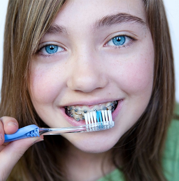 Young girl brushing teeth with toothbrush, smiling outdoors in dental care context.