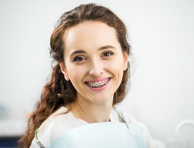 Smiling woman in white shirt against neutral background, orthodontic patient portrait.
