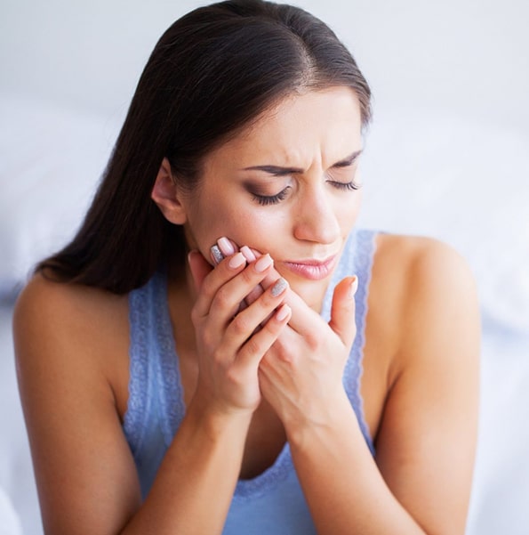 Woman holding her cheek in pain, appearing to have tooth or jaw discomfort.