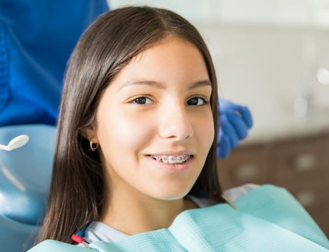 Young girl smiling at camera wearing dental bib in orthodontic office setting.