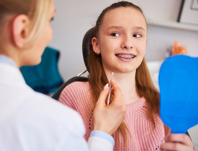 Orthodontist showing blue mirror to smiling young patient during dental examination in clinic.