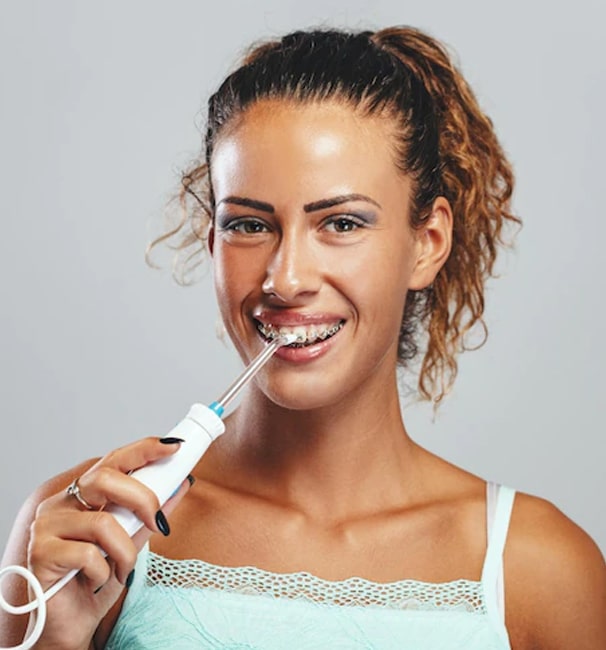 Young woman smiling while holding electric toothbrush against gray background.