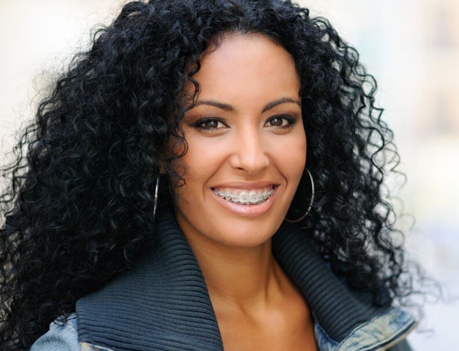 Professional woman with long curly black hair smiling at camera, wearing dark blazer.