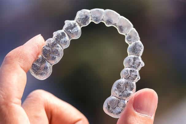Clear plastic orthodontic aligner held in hand against blurred background, demonstrating modern invisible braces technology.