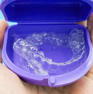 Clear plastic orthodontic retainers displayed in purple storage case.