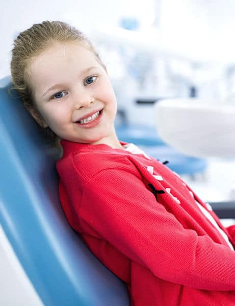 Young girl smiling in dental chair wearing pink shirt at orthodontic office.