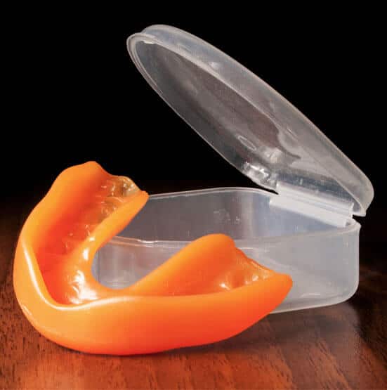 Clear plastic orthodontic mouthguard with orange athletic mouth protector displayed next to open case.