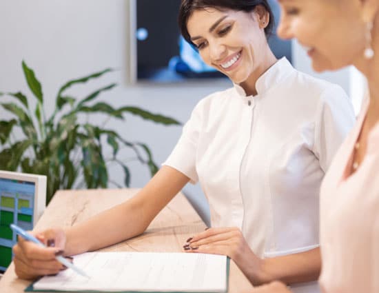 Orthodontist in white coat showing patient treatment plan at dental office desk.