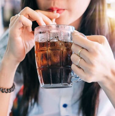 Young woman drinking cola from clear cup with straw indoors