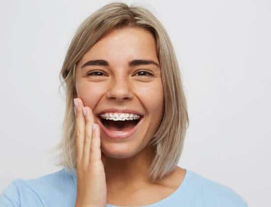 Woman smiling brightly while touching her face, wearing blue shirt against white background.