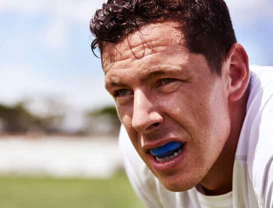 Athletic man wearing blue mouthguard on outdoor sports field during daytime.