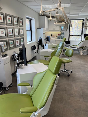 Modern orthodontic treatment room with green dental chairs, overhead lighting, and framed certificates on walls.