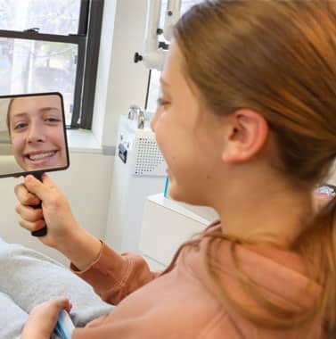 Patient examining her smile in handheld mirror during orthodontic consultation at dental office.