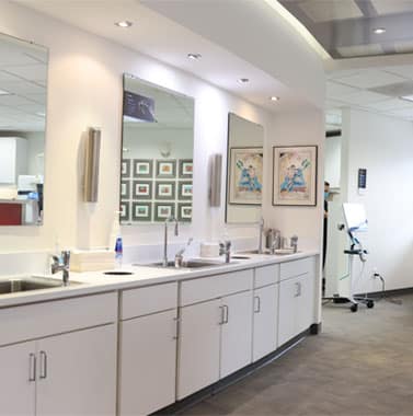 Modern orthodontic office treatment area with white cabinetry, large mirror, and dental equipment.