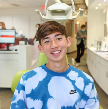 Smiling young teen wearing blue and white patterned shirt in orthodontic office waiting area.