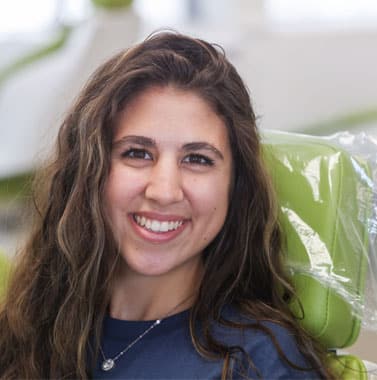 Smiling woman with long dark hair in professional headshot, indoor setting with plants.