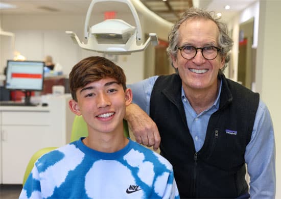 Orthodontist and young patient smiling together in dental office treatment room.