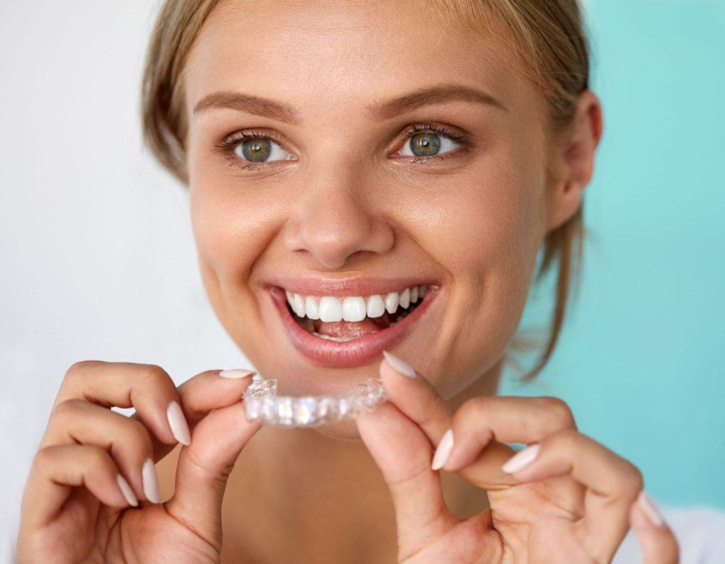 Young woman smiling while holding clear aligner trays against turquoise background.