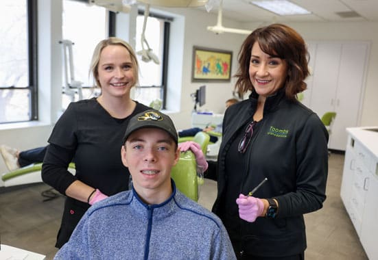 Three smiling staff members pose together in a bright orthodontics office reception area.