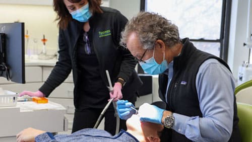 Two dental professionals wearing masks examine orthodontic equipment in a clinical setting.