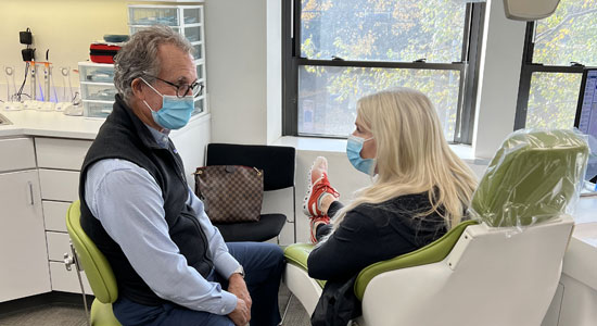 Orthodontist in mask discussing treatment with female patient in bright clinical office setting.