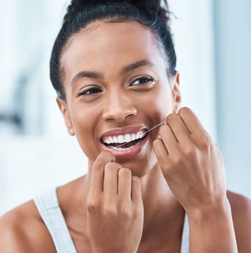 Smiling woman applying skincare product to face in bright, clean bathroom setting.