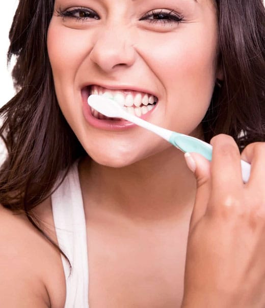 Young woman smiling brightly while brushing teeth with toothbrush against white background.
