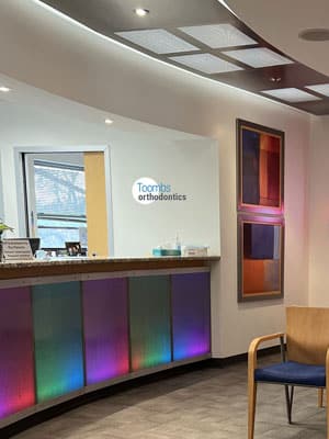 Modern orthodontic office reception area with colorful front desk and contemporary waiting chair.