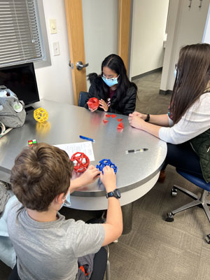 Three children and an adult examine colorful 3D-printed orthodontic models at a table in an office setting.