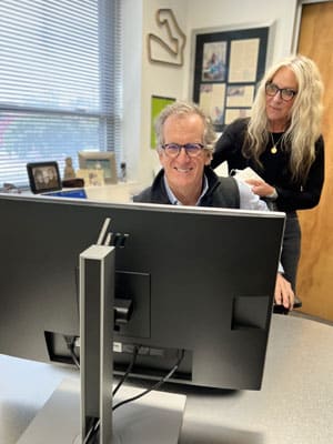 Two team members at Toombs Orthodontics smiling at computer monitor in office setting.