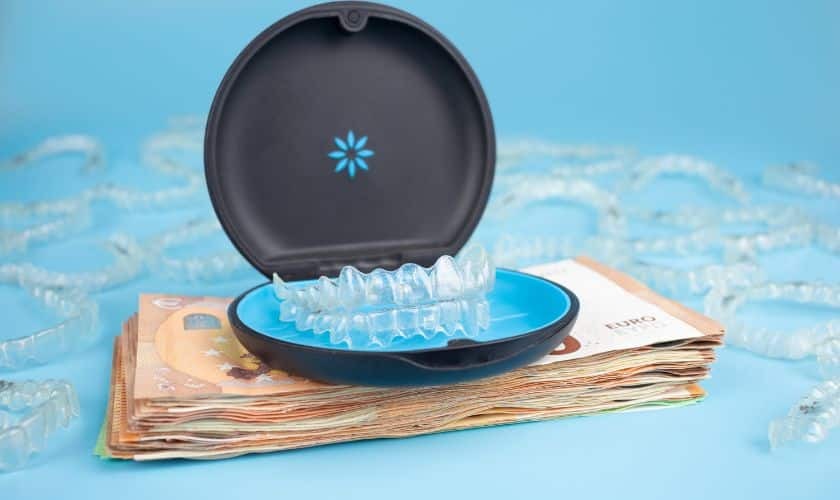 Invisalign clear aligners displayed in an open case on a stack of money, symbolizing investment in orthodontic treatment.
