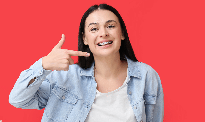 Smiling woman pointing to her teeth against a red background, representing adult orthodontic treatment results.