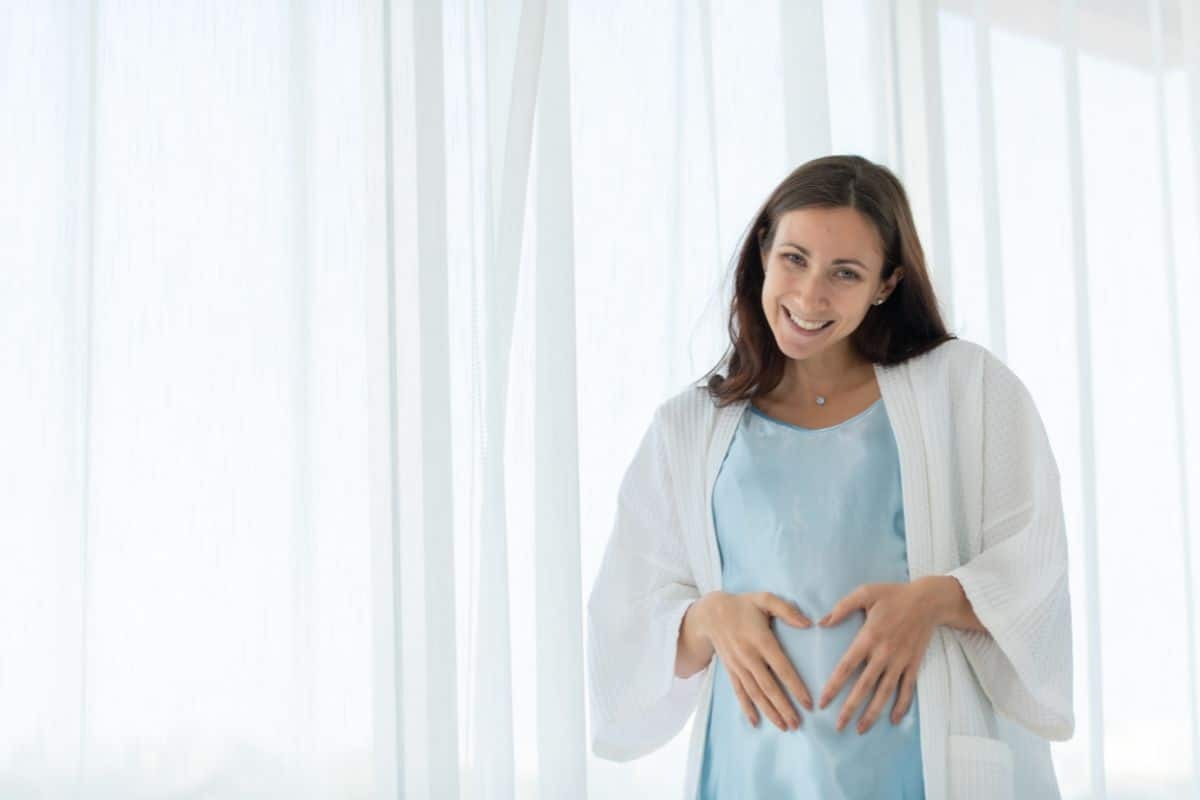 Pregnant woman smiling with hands on belly during dental consultation.