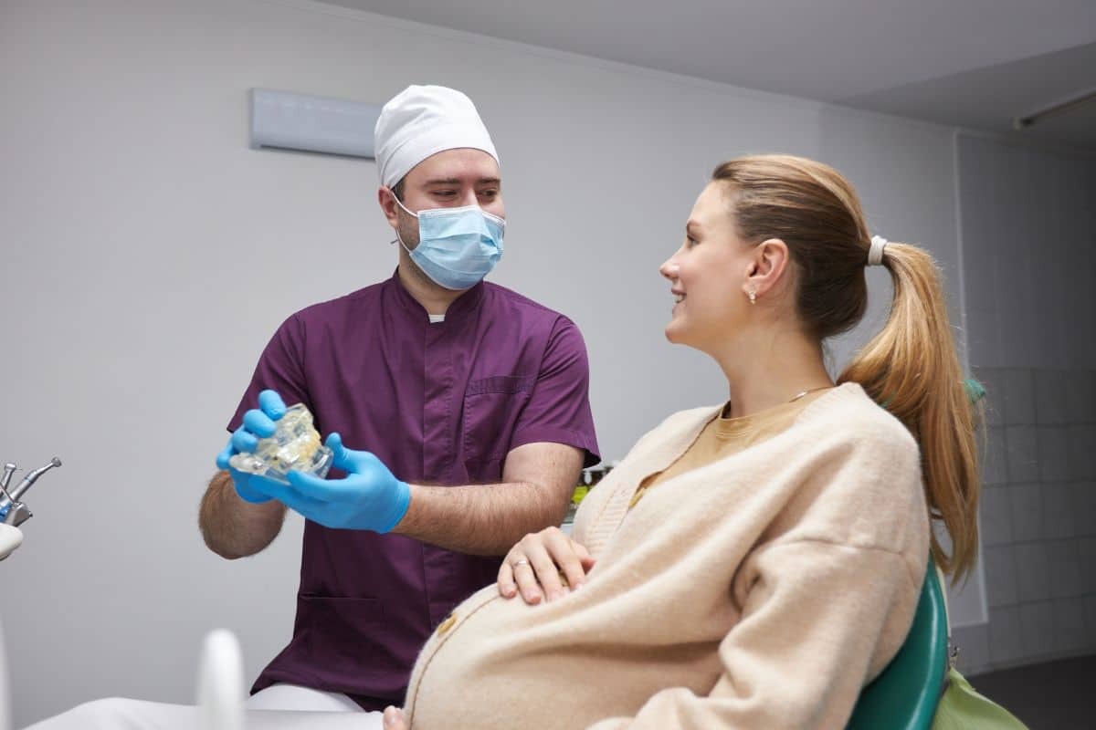 Pregnant patient smiling while male dentist shows dental model during orthodontic consultation.