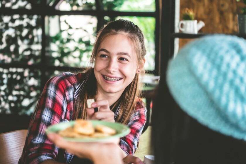 Happy young patient with braces enjoying healthy food, supporting orthodontic progress.
