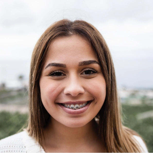 Smiling teenage girl with braces outdoors against blurred landscape background.