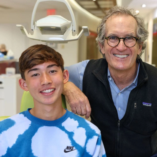 Young patient and orthodontist smiling together in dental office treatment room.