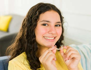 Smiling woman in yellow shirt holding green apple in bright, modern living room setting.