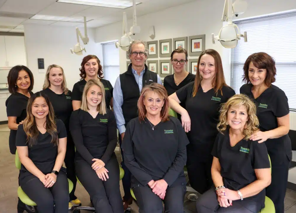 Toombs Orthodontics team of dental professionals posing together in modern office setting wearing black uniforms.