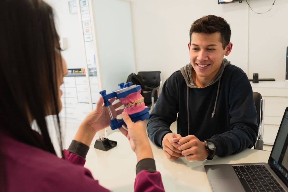 Teenage boy smiling while discussing dental model with female patient in orthodontic office.