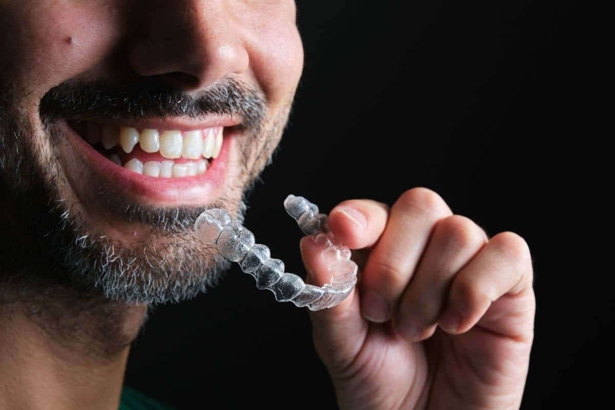 Man holding clear Invisalign aligner tray while smiling, showing teeth alignment treatment progress.