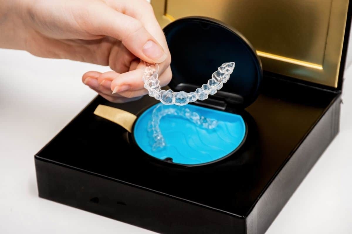 Hand holding clear Invisalign aligner over blue storage case showing proper orthodontic treatment care.